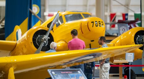 A group of people observing a yellow vintage aircraft with the number 7862 displayed on its nose, inside an aviation museum.